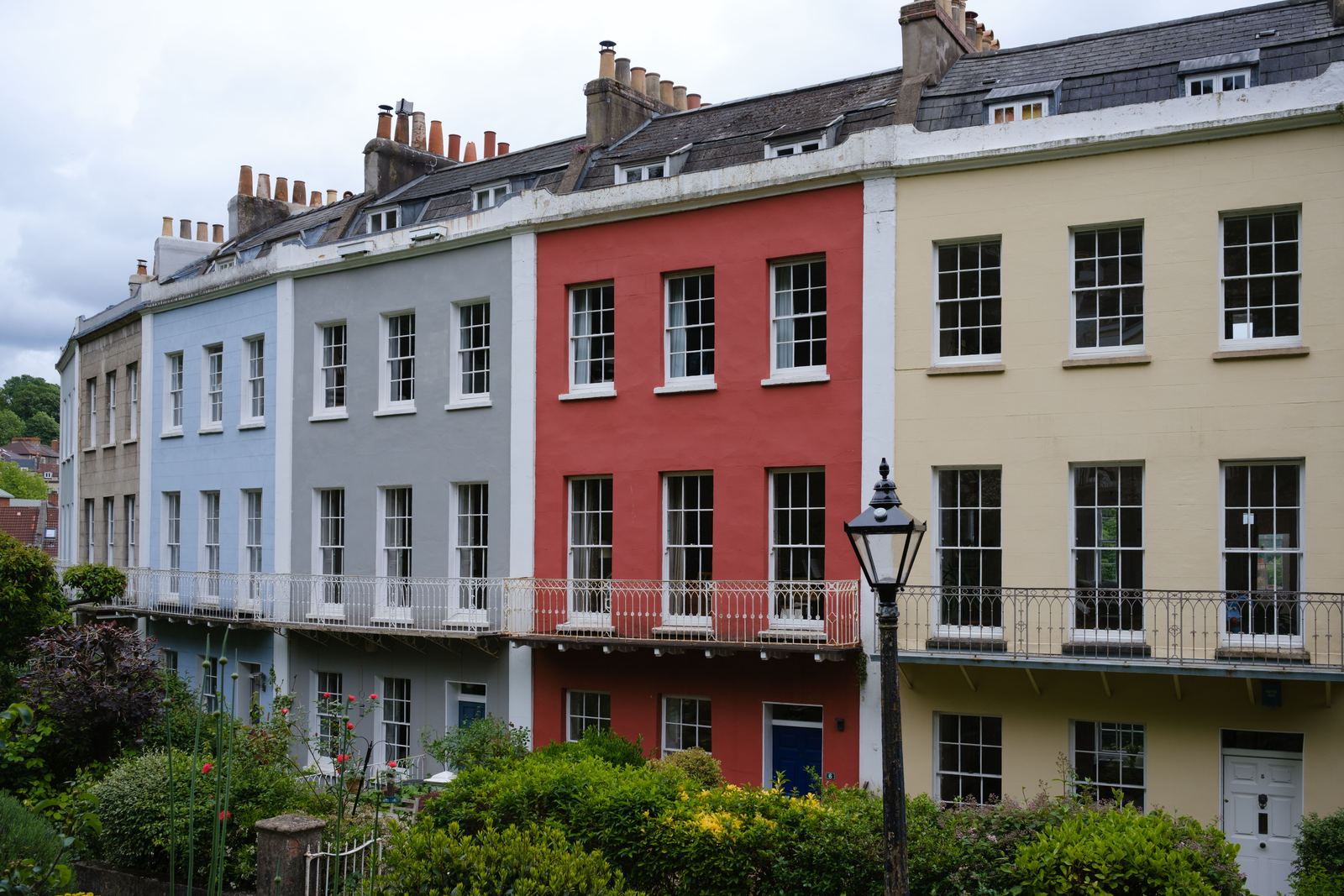 Row of painted terraced townhouses in blue, grey, red and cream with iron balconies and chimney stacks