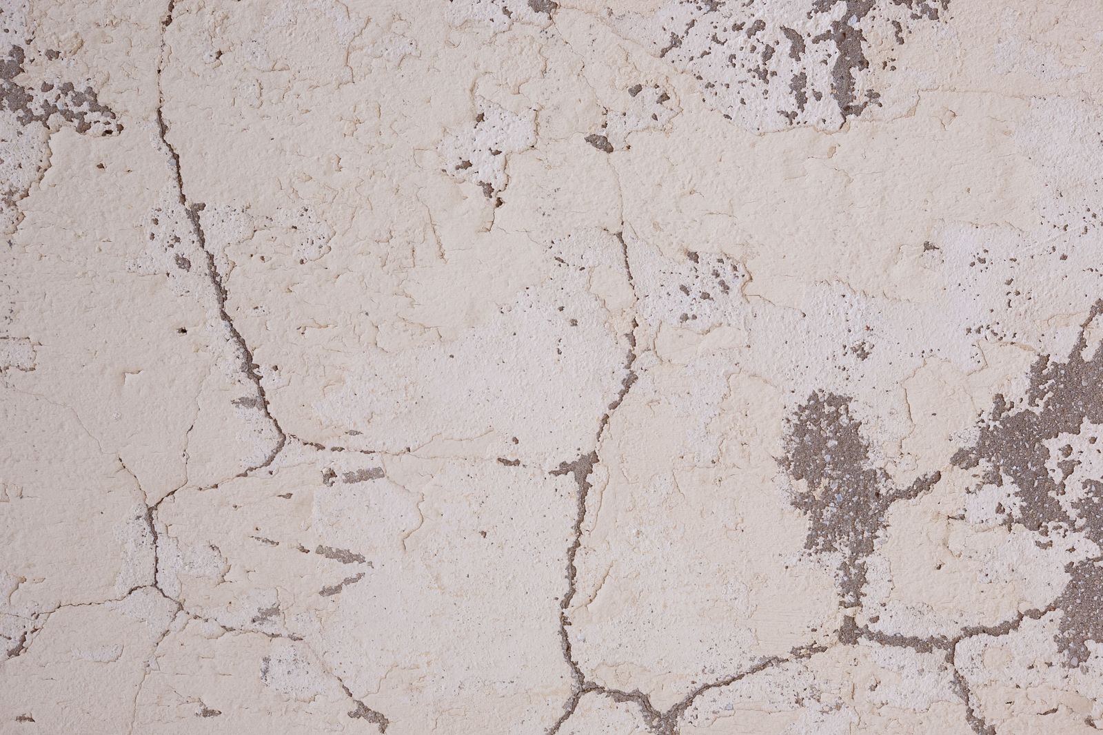 Close-up of cracked, flaking cream plaster on a wall with grey patches showing through