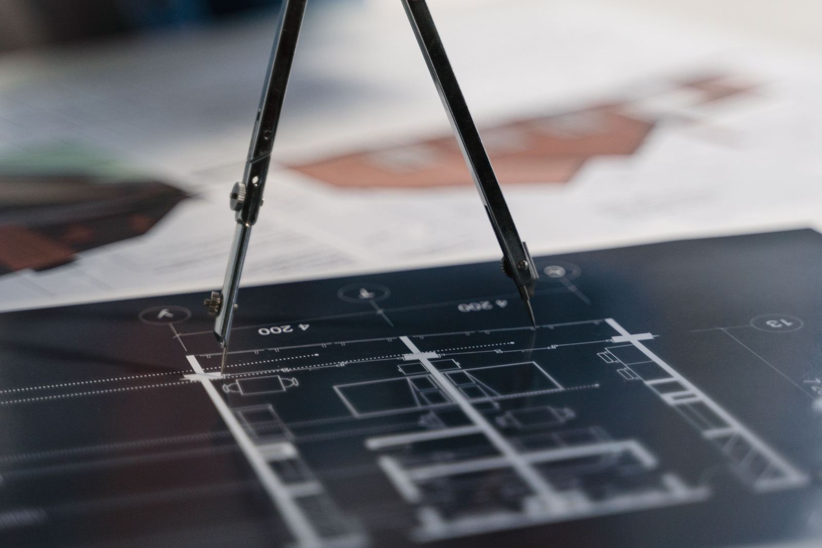 Pair of drawing compasses resting on an architectural floor plan printed on dark paper