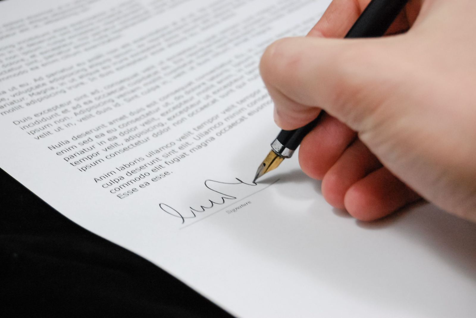 Hand signing the signature line of a printed document with a fountain pen