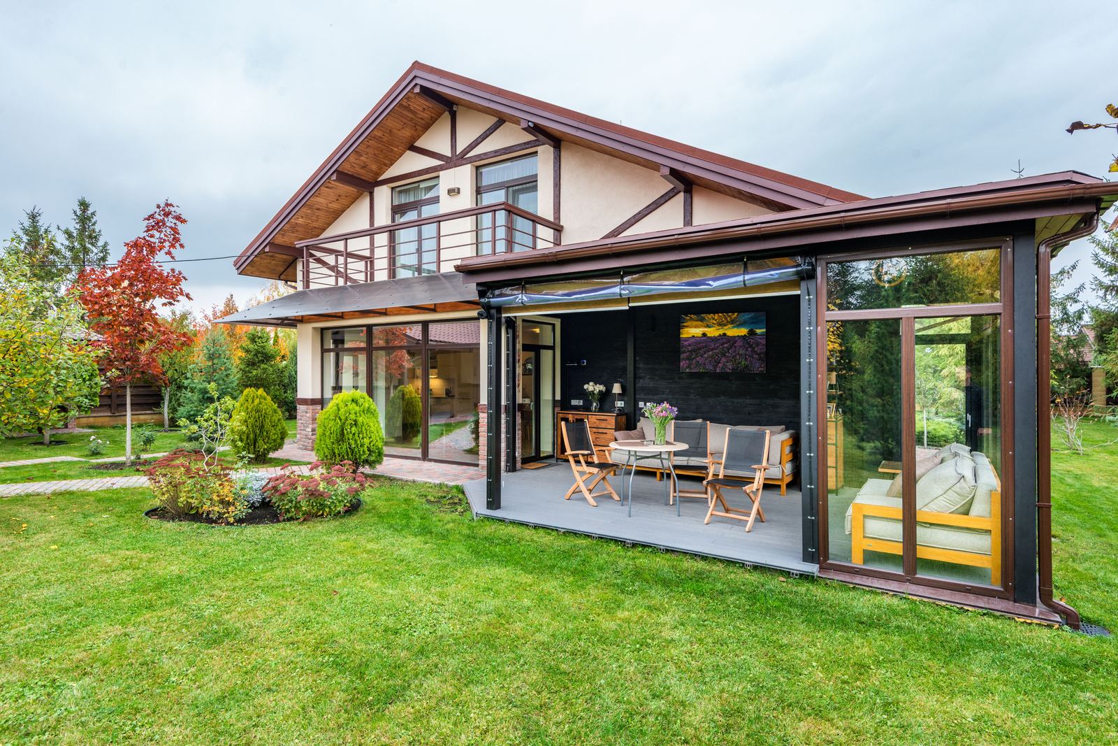 A glazed garden room with large glass panels attached to the side of a house, on a lawn