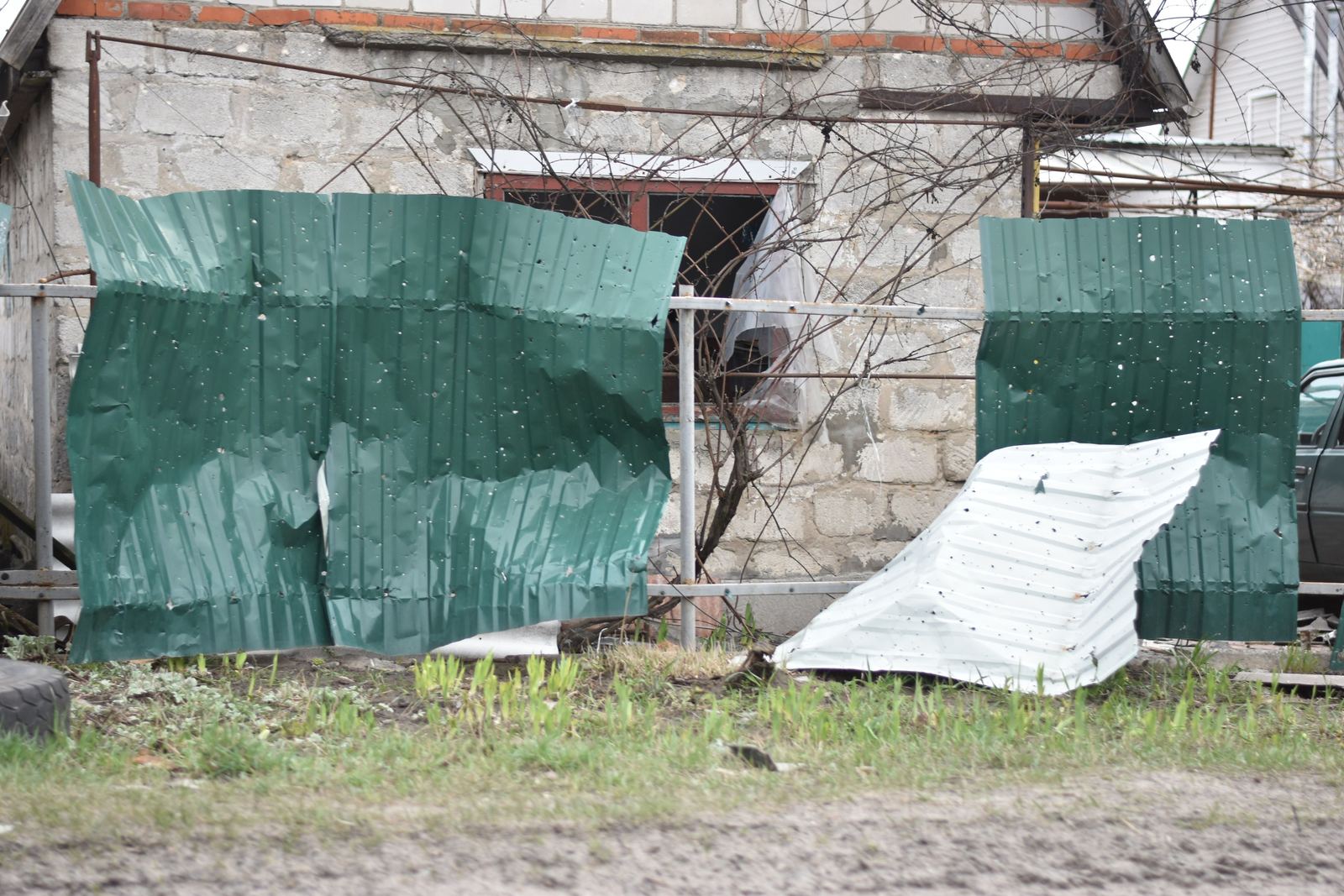 Bent green and white corrugated metal sheets propped against a railing outside a block-built house