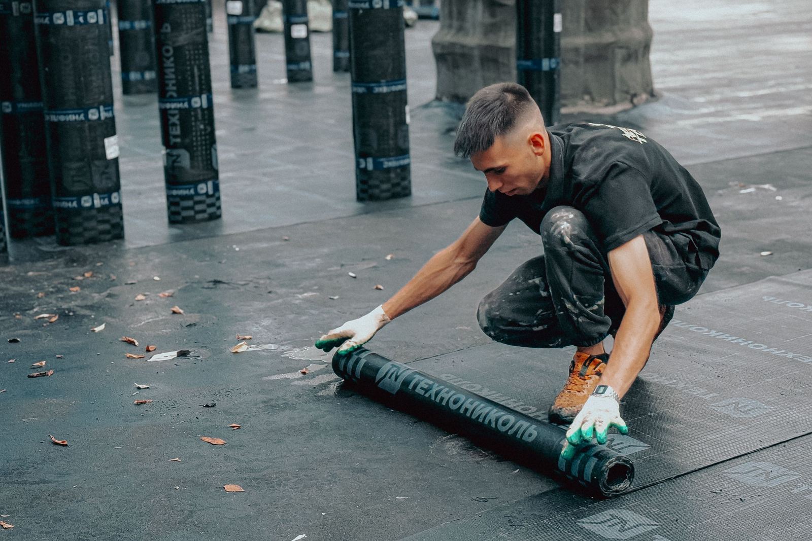 A roofer kneeling on a flat roof, unrolling a new roll of waterproof membrane