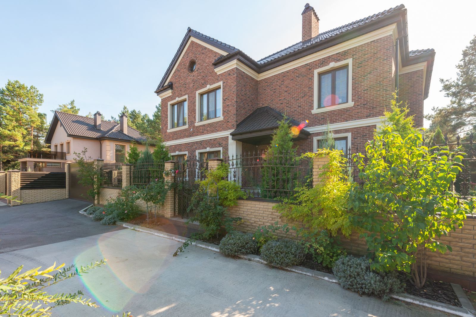 Large red brick house behind a low brick front wall with iron railings and shrubs