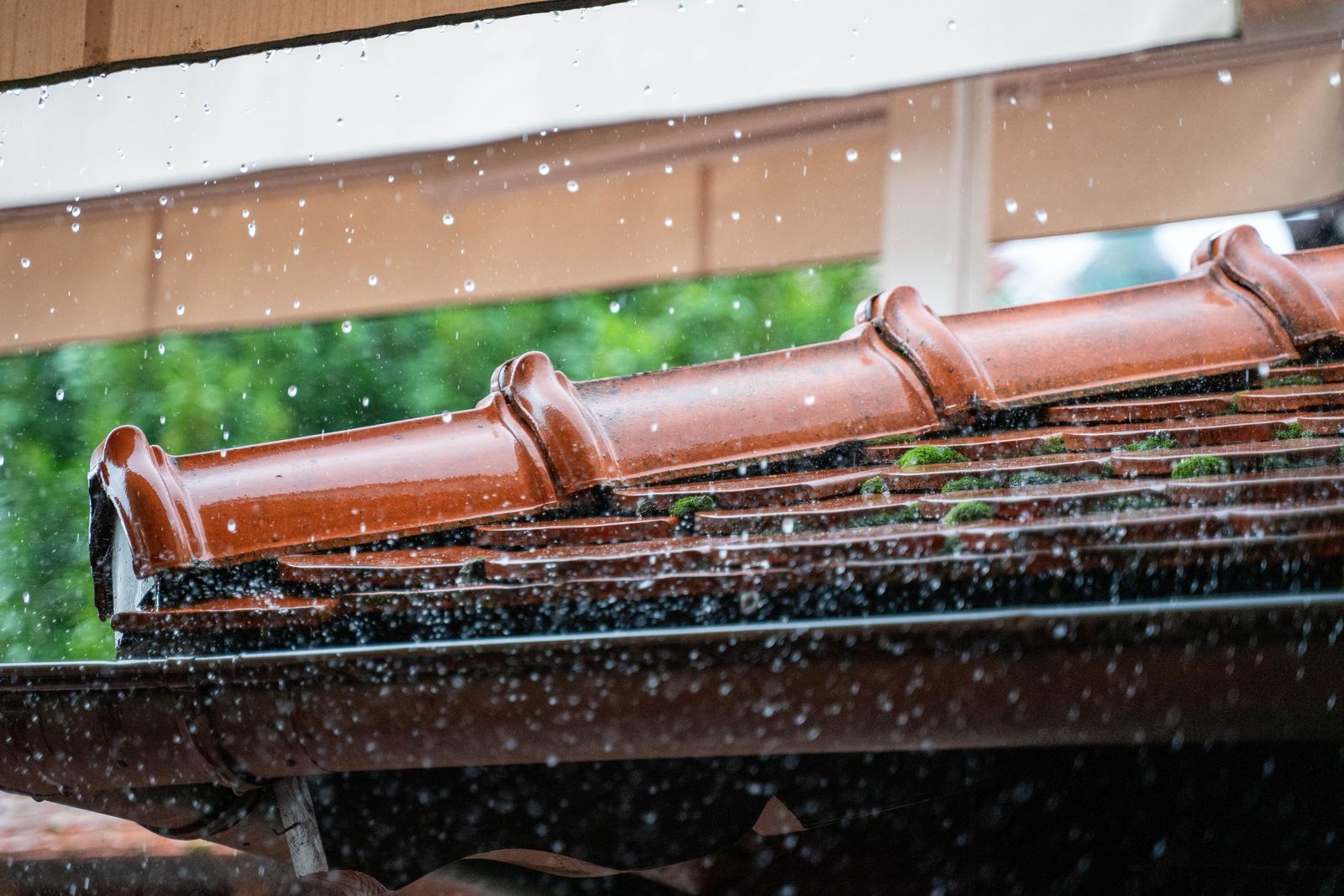 Rainwater spilling over the front edge of a blocked gutter during heavy rain