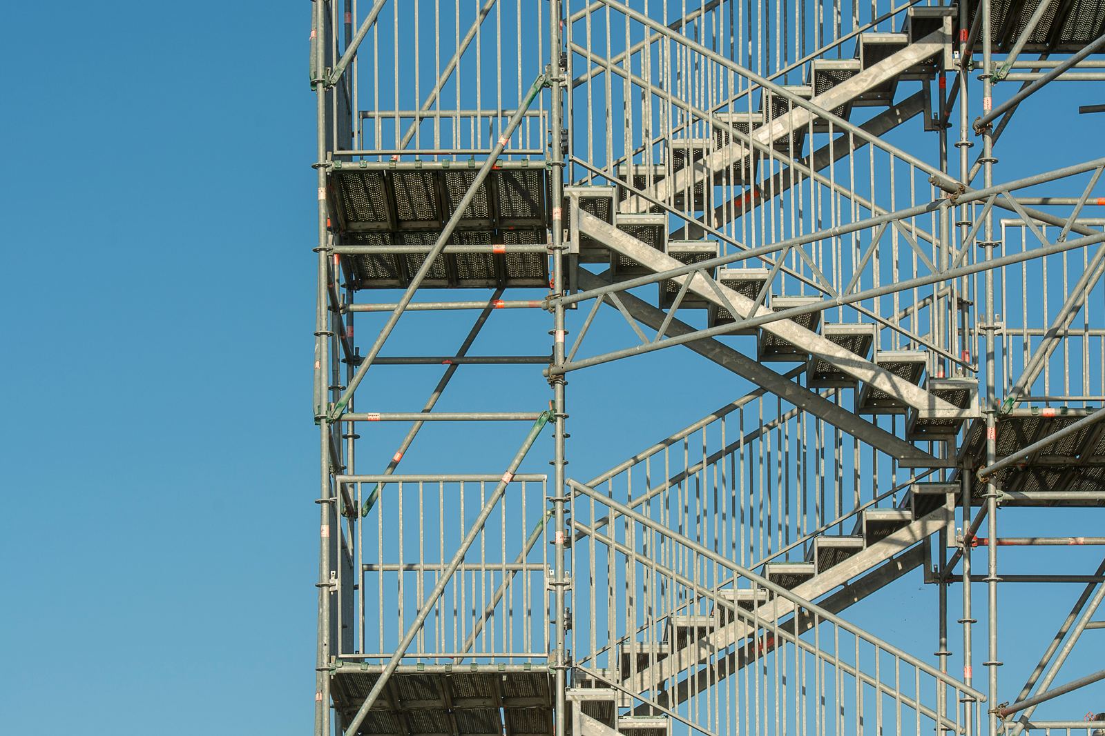 Metal scaffold tower with zigzag stairways and guardrails against a clear blue sky