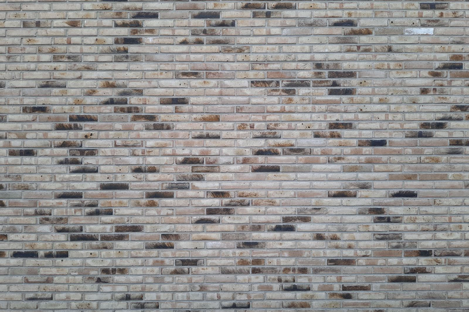 Wall of pale, mixed-tone bricks with thin light mortar joints and scattered darker bricks