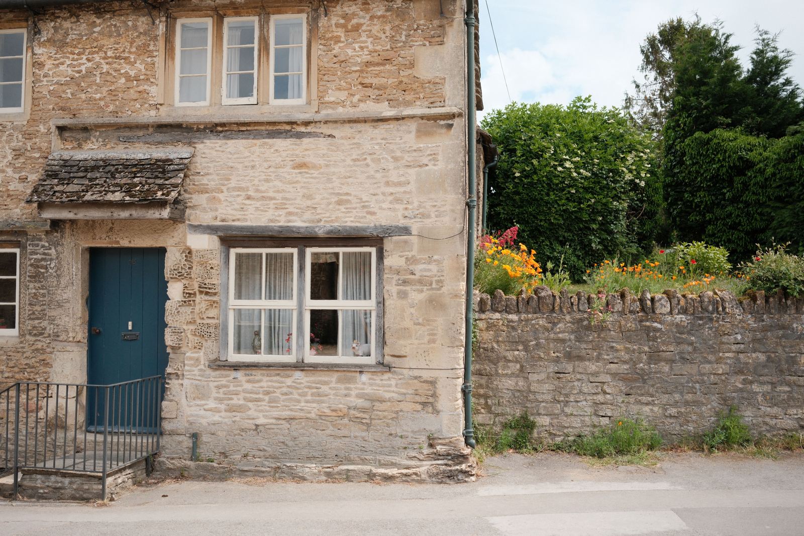 Old limestone cottage with a blue front door, mullioned windows and a dry stone boundary wall