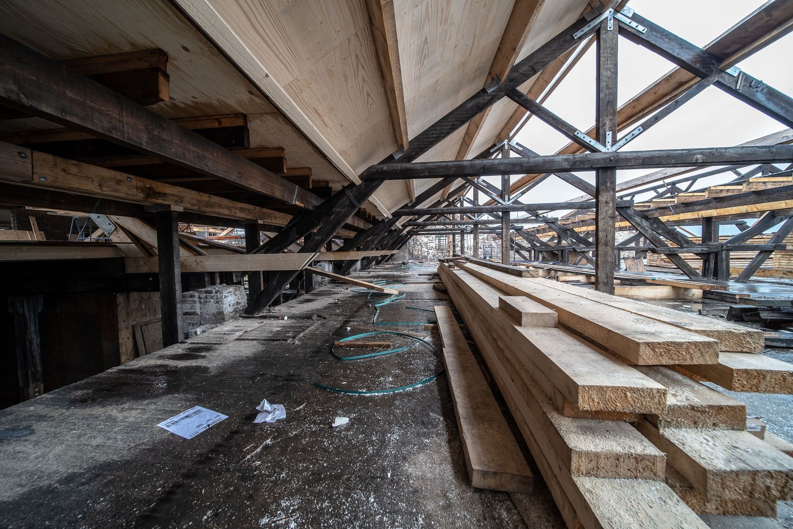 Exposed timber roof trusses in a large open roof space with stacked new boards on the floor