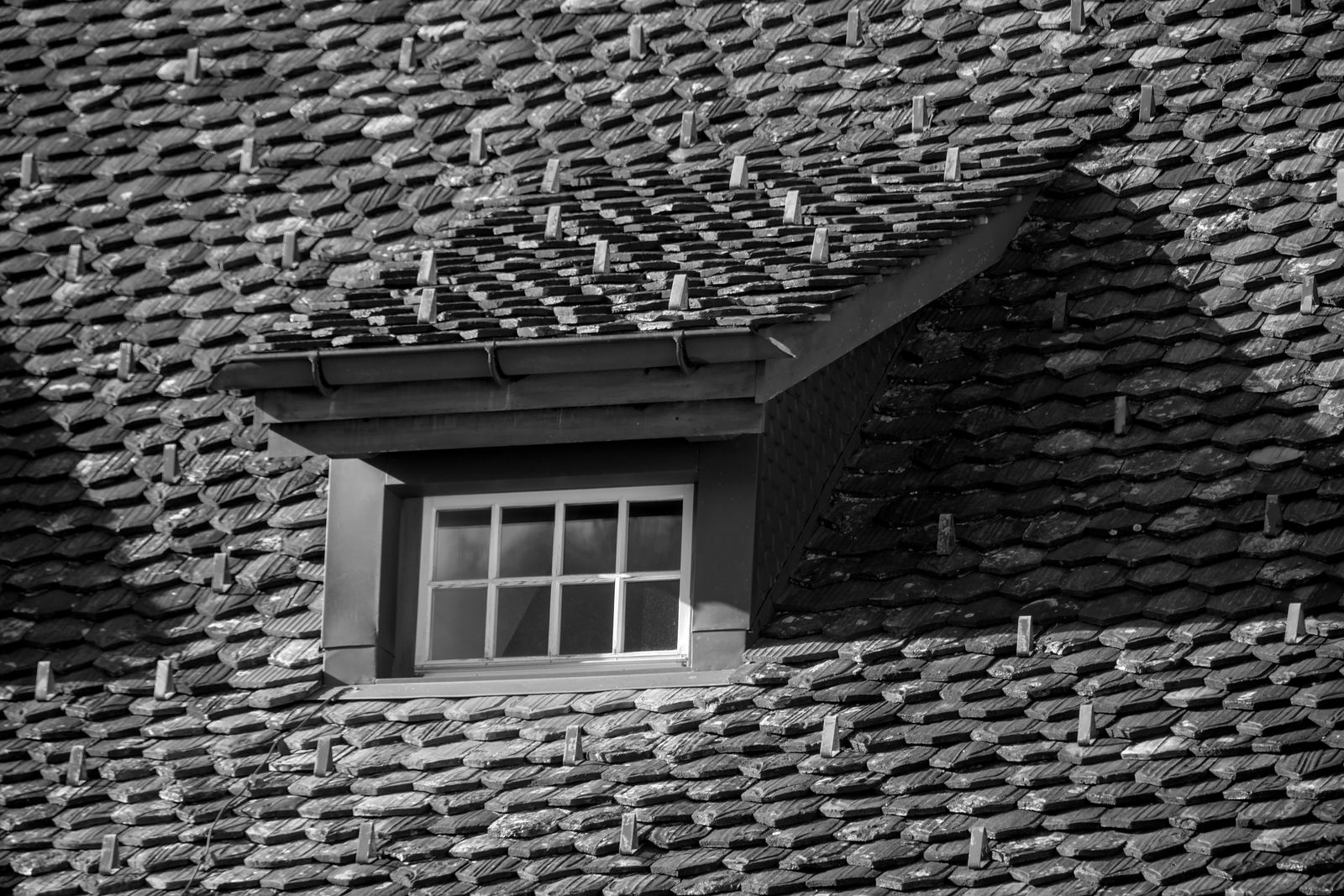 Black and white close-up of a small dormer window in a roof of overlapping tiles