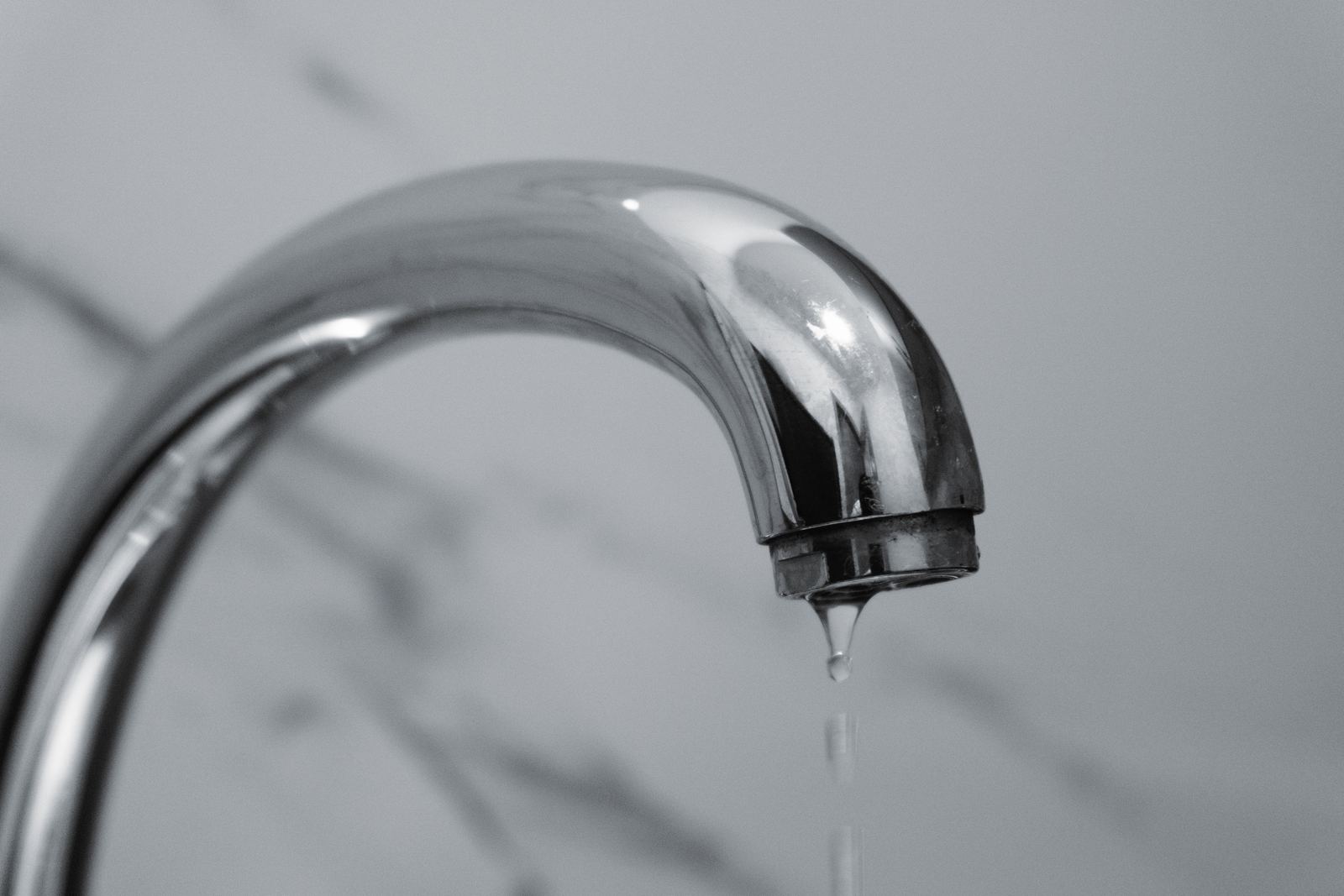 Black and white close-up of a water drop falling from a chrome tap spout