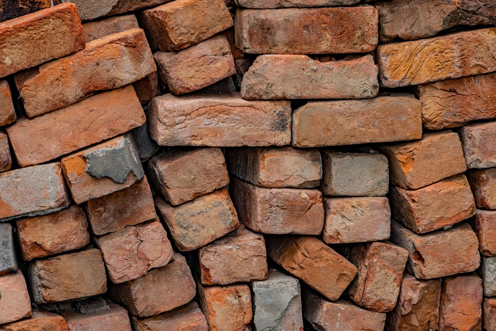 Stack of weathered, chipped old red bricks with traces of mortar
