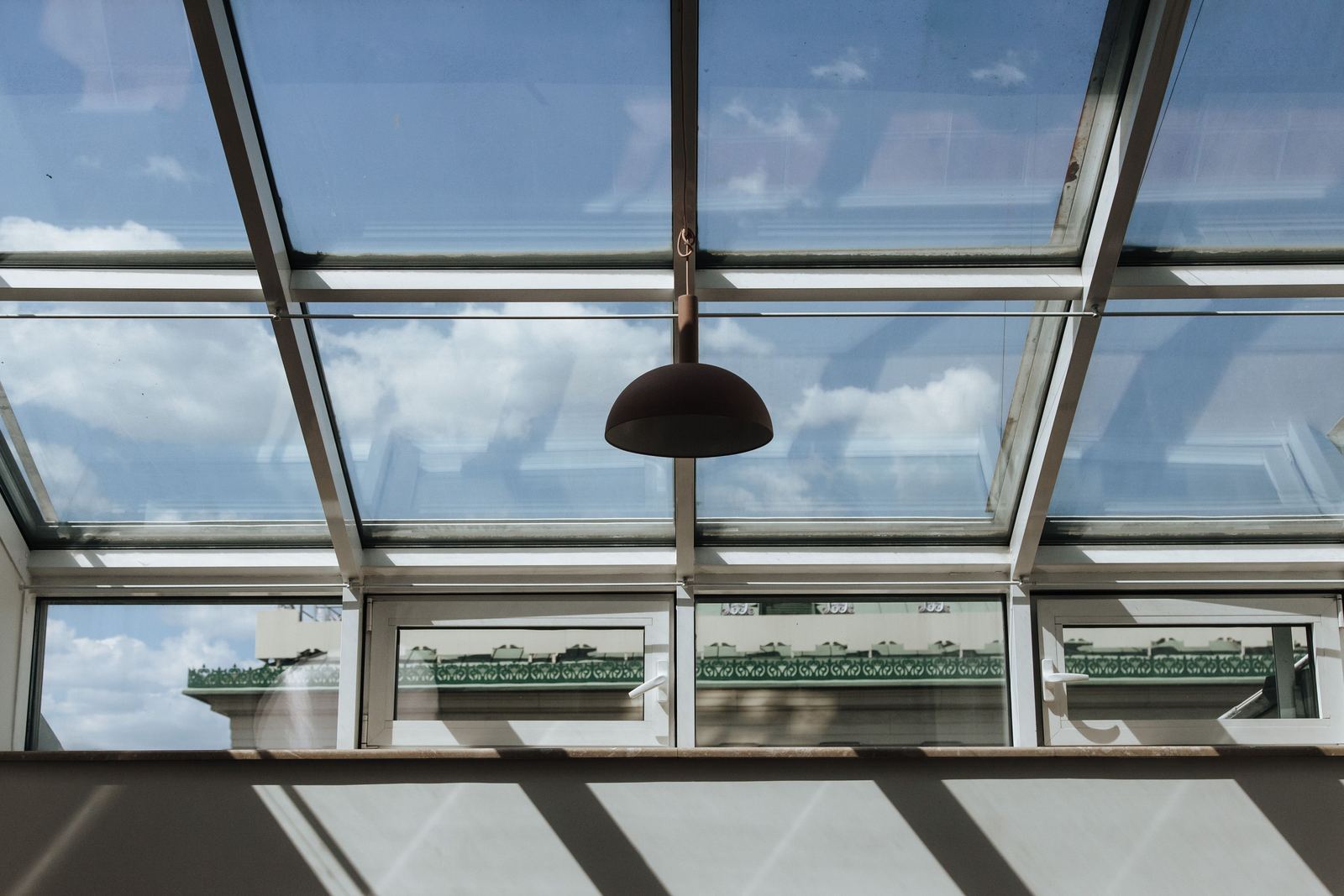Looking up through a glazed roof of clear panels in white frames, with a pendant light hanging from the ridge