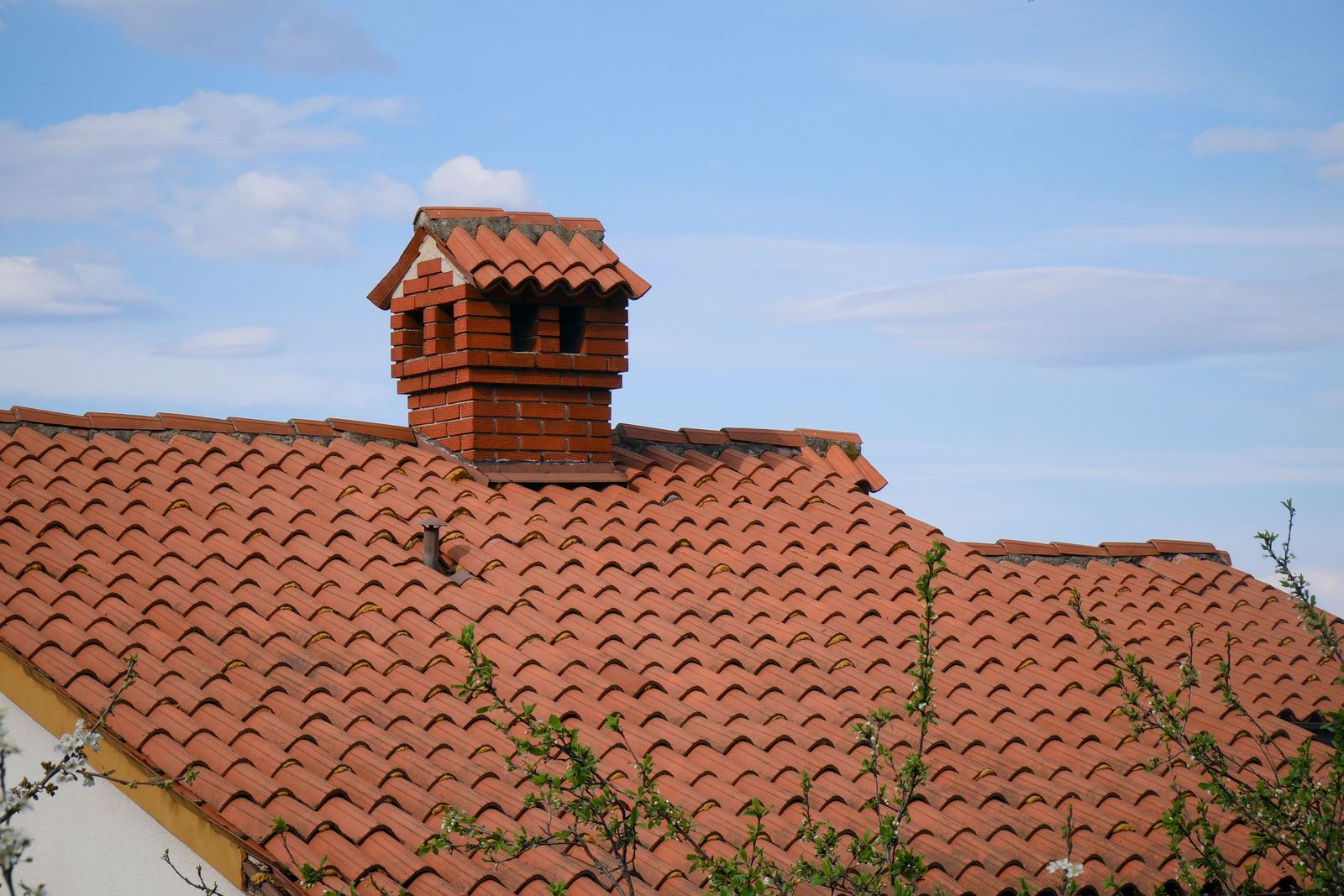 A tiled pitched roof with a brick chimney, against a blue sky