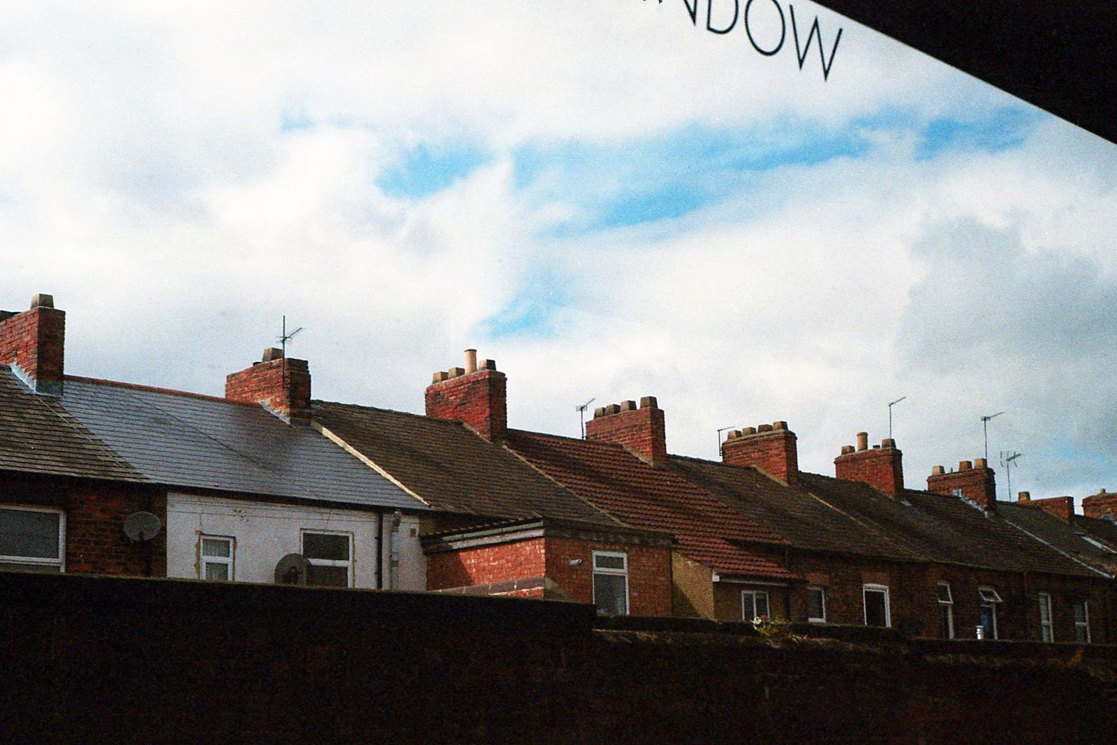 Row of terraced house roofs with brick chimney stacks and TV aerials under a cloudy sky