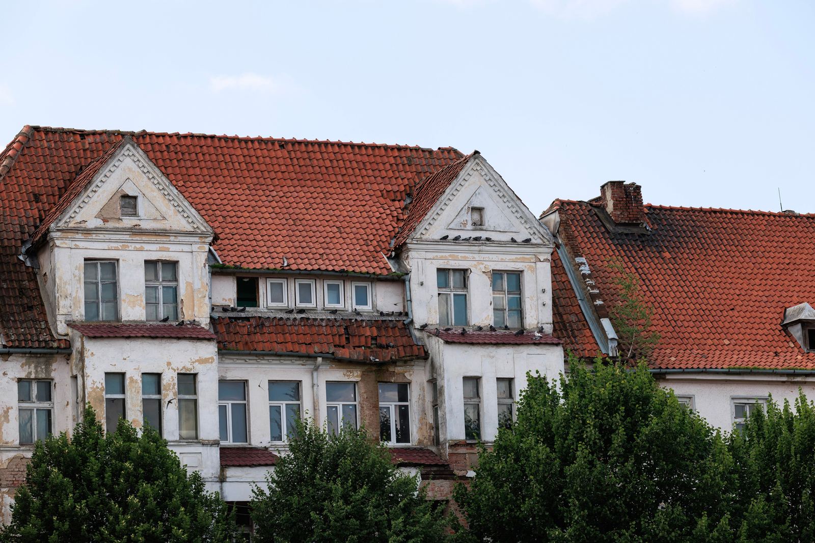 Weathered old building with patchy red clay tile roofs, gabled dormers and peeling white walls