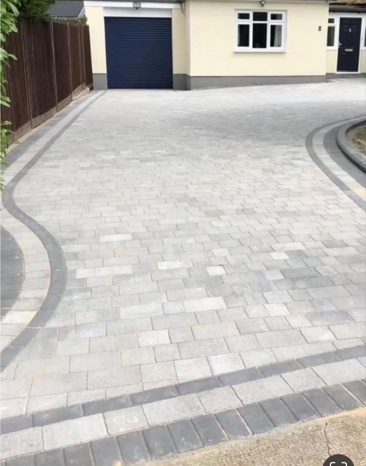 Block paved driveway seen from the road end, with the garage and front door of a cream rendered house