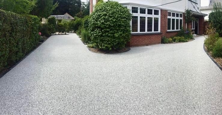 Light grey resin bound driveway sweeping past a clipped hedge to a red brick house