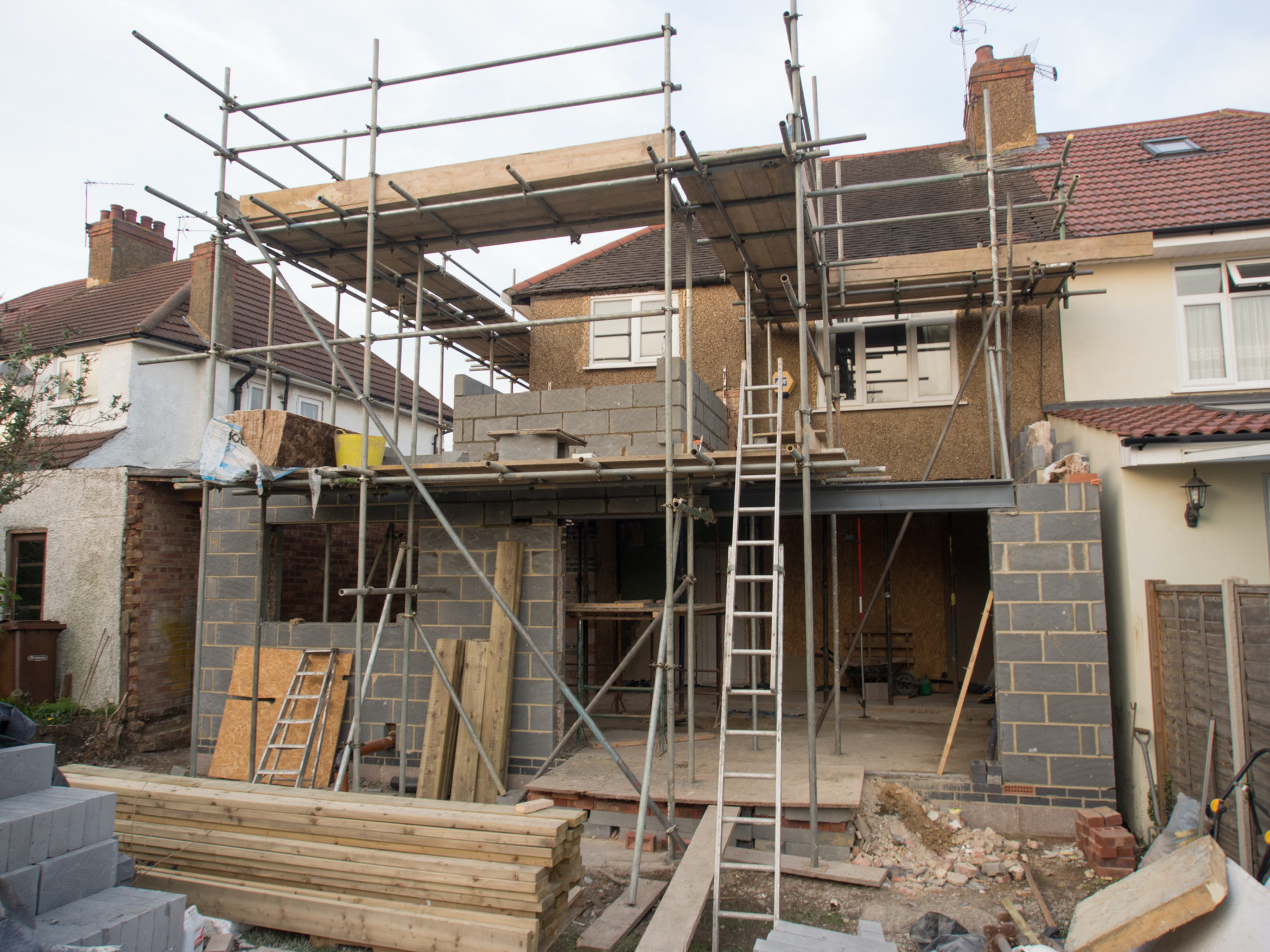 Two-storey rear house extension under construction with scaffolding, blockwork walls and a steel beam