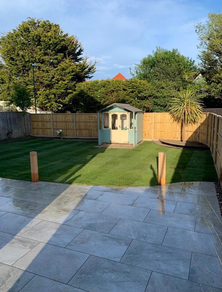 Grey porcelain patio in the foreground with a striped lawn running back to a summerhouse