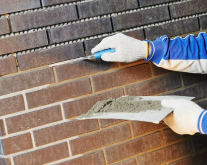 Gloved hands working fresh mortar into a raked-out joint on an old brick wall
