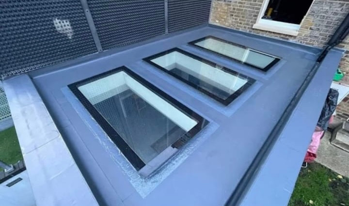 Finished grey GRP flat roof with three rooflights, formed upstands and the fall running to the outlet