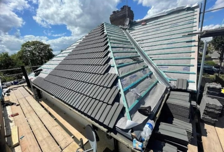 Hipped roof part way through a retile, with breather membrane and battens exposed on one side